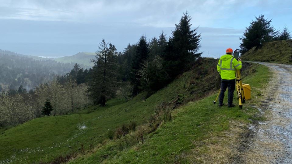 A surveyor at work on the shoulder of a county road.