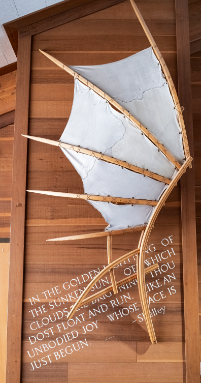 A curved wooden and canvas sculpture mounted on a redwood wall.