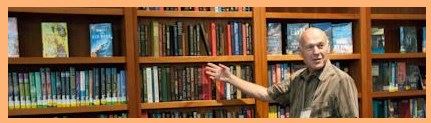 Image, a man gesturing to a bookshelf.  