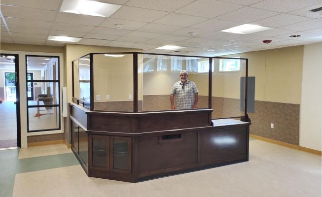 A carpenter stands inside the new service desk, built of wood with a glassed-in top. 
