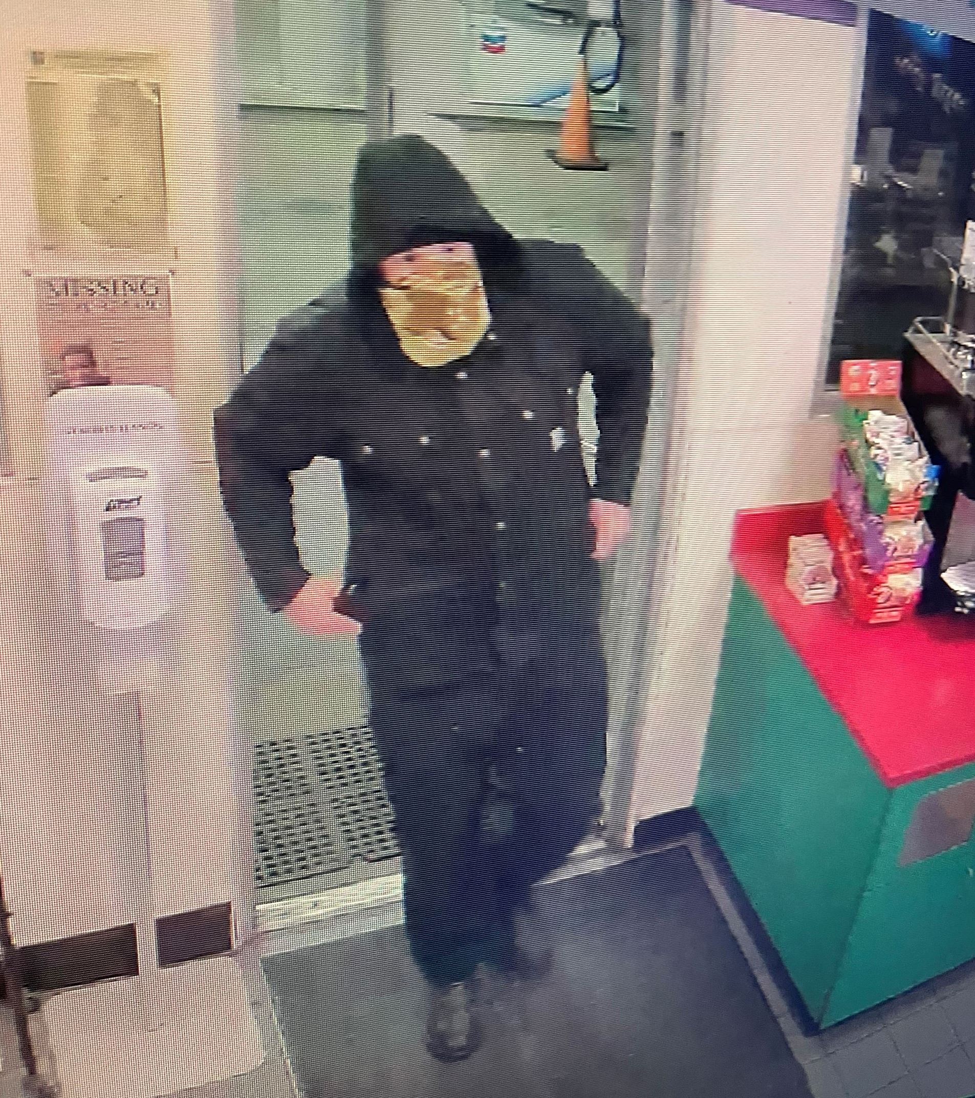 White male adult wearing a black hooded zip-up jacket, black pants and a neck gaiter mask