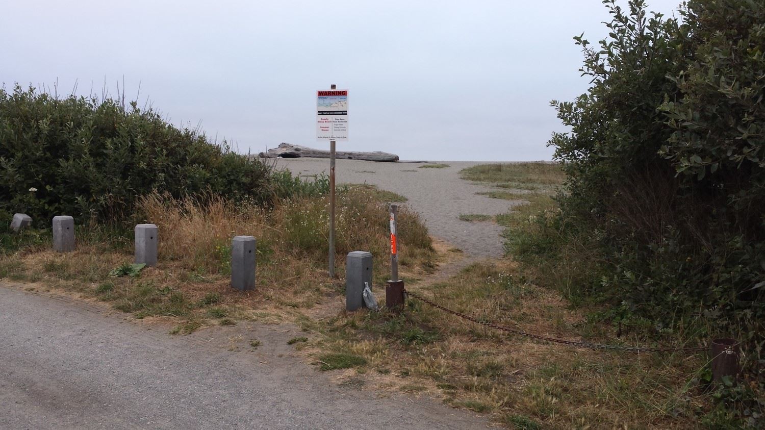 Sign posted between parking lot and beach, next to trail